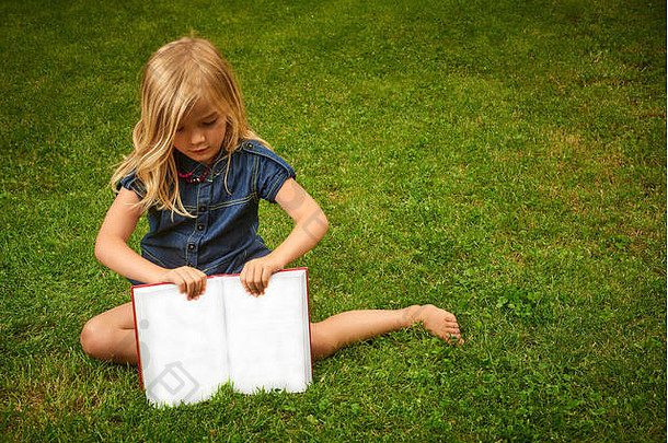 可爱的金发碧眼的女孩阅读书草