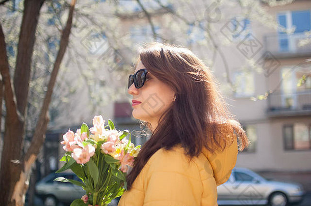 在户外肖像时尚的有吸引力的浅黑肤色的女人女人太阳镜走在户外大花束色彩斑斓的花阳光明媚的春天一天