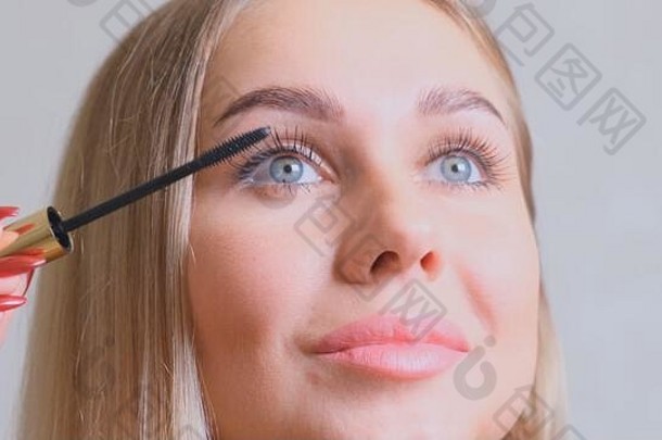 漂亮的金发碧眼的女人应用睫毛膏化妆睫毛前面镜子美化妆概念