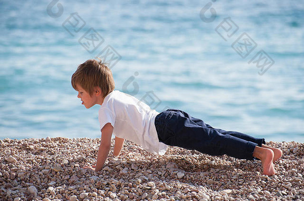 可爱的健康的强大的孩子使俯卧撑努力海海岸秋天锻炼