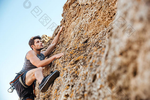 年轻的英俊的运动员攀爬岩石悬崖