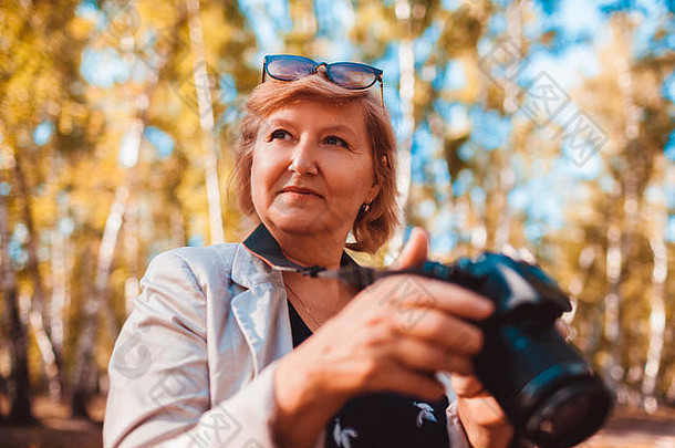 中年女人检查图片相机秋天森林高级女人走享受爱好