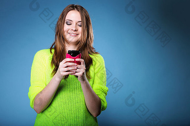 快乐微笑女孩移动电话智能手机读取消息工作室拍摄蓝色的背景