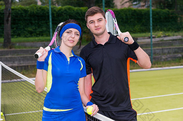年轻的夫妇网球球员穿运动服装持有球拍肩膀球手站户外