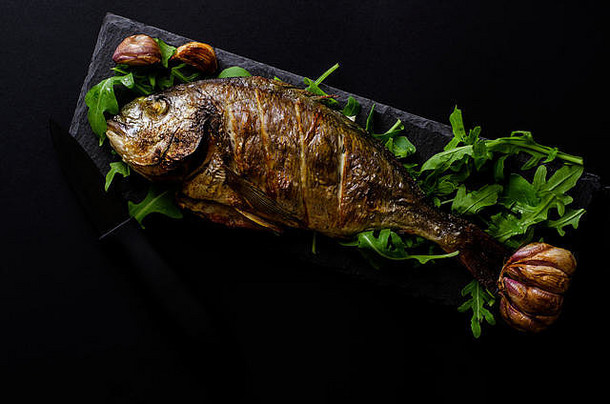 烤多拉达鱼新装的芝麻菜黑色的背景黑暗食物照片海鲜概念开销拍摄复制空间
