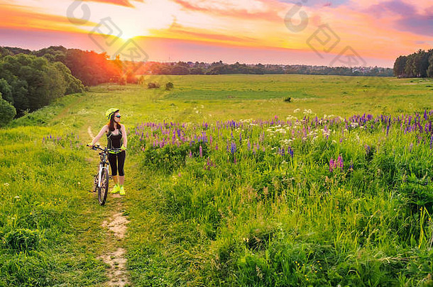年轻的运动女人骑自行车日落运动女孩艰苦的自行车享受美丽的场卢平镜头耀斑天空背景