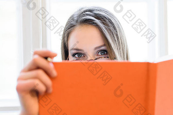 美丽的金发女郎学生女孩覆盖脸橙色书