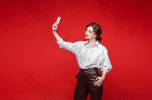 英俊的女持有电话需要自拍图片孤立的红色的背景