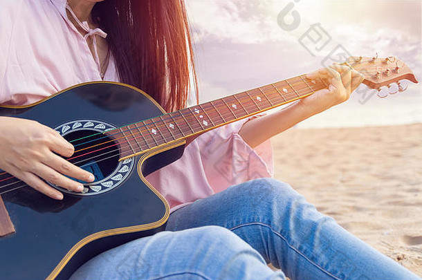 女人的手玩声吉他捕获和弦手指桑迪海滩日落时间玩音乐概念