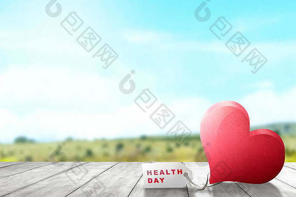 红色的心白色纸标签木表格健康一天消息绿色场蓝色的天空背景健康一天概念
