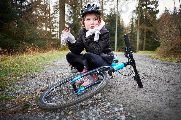 年轻的女孩坐在自行车吃零食森林跟踪
