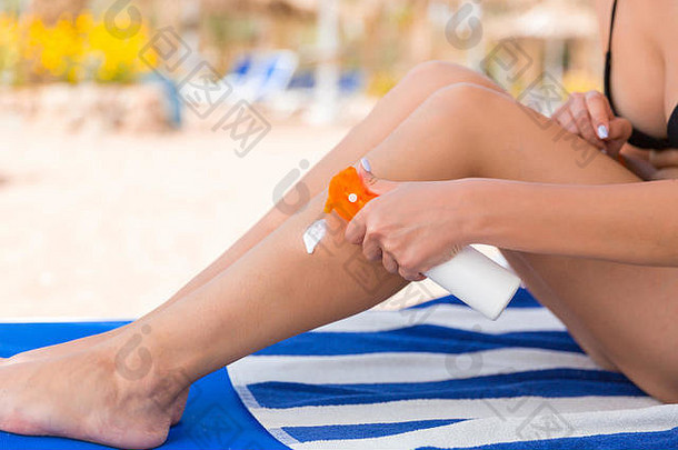 女孩坐着日光浴浴床应用太阳奶油腿海滩