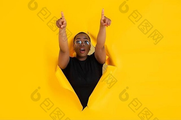 指出快乐的非裔美国人年轻的女人提出了撕裂黄色的纸背景情感富有表现力的打破breakthrought概念人类情绪面部表达式销售