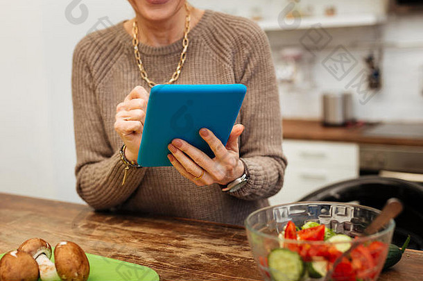 成熟的夫人米色温暖的毛衣携带蓝色的平板电脑