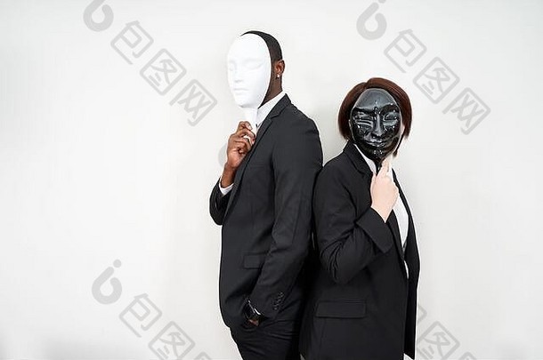 非洲男人。高加索人女人穿黑色的西装隐藏脸塑料面具
