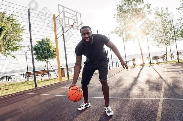在户外活动非洲男人。玩篮球法院运球微笑兴奋