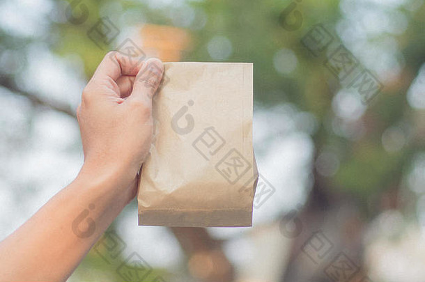 关闭女持有手棕色（的）清晰的空空白工艺纸袋模糊散景自然背景包装袋
