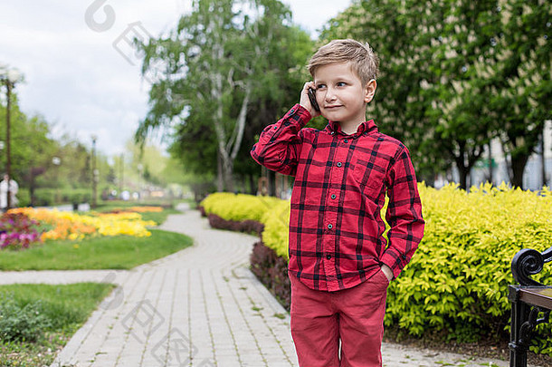 男孩红色的衬衫会说话的细胞电话在户外男孩微笑