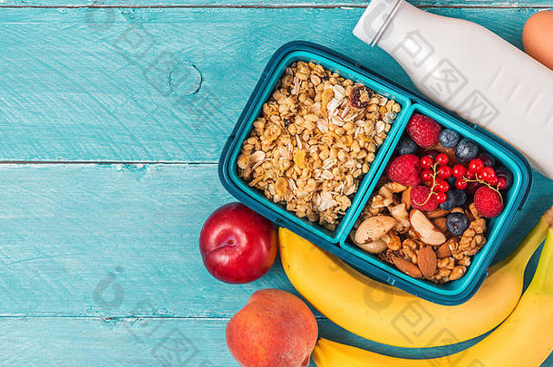 健康的午餐盒子格兰诺拉麦片坚果浆果香蕉鸡蛋桃子酸奶使早餐蓝色的背景前视图复制空间