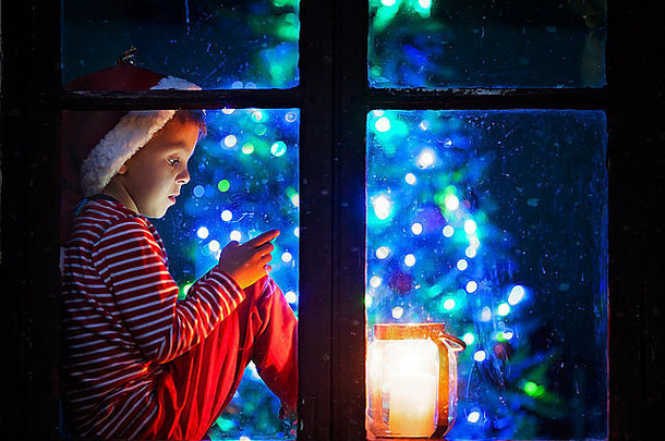 可爱的男孩坐着窗口盾玩移动电话晚上圣诞节时间等待圣诞老人老人