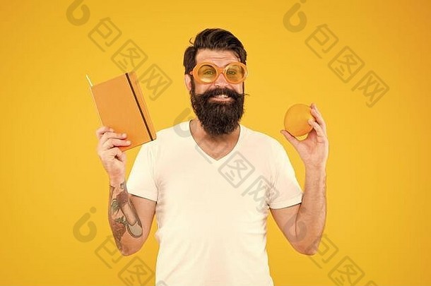 明亮的充满活力的男人。有胡子的快乐的微笑赶时髦的人穿橙色颜色太阳镜持有橙色水果书记事本总计橙色的家伙长胡子喜欢橙色颜色维生素源
