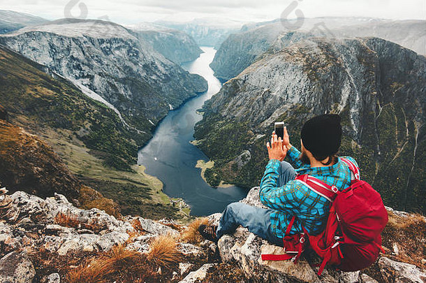 男人。旅行者智能手机坐着山峰会旅行挪威冒险生活方式活跃的假期现代技术连接概念