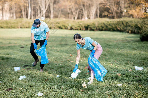 男人。女人志愿者穿着蓝色的t恤清洁公共花园塑料垃圾袋
