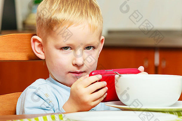 快乐童年金发碧眼的男孩孩子孩子吃玉米片麦片牛奶早餐早....餐玩移动电话