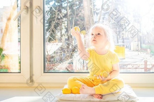 女孩<strong>黄色</strong>的<strong>衣服</strong>柠檬手坐在窗台上下午微笑明亮的太阳照柑橘类