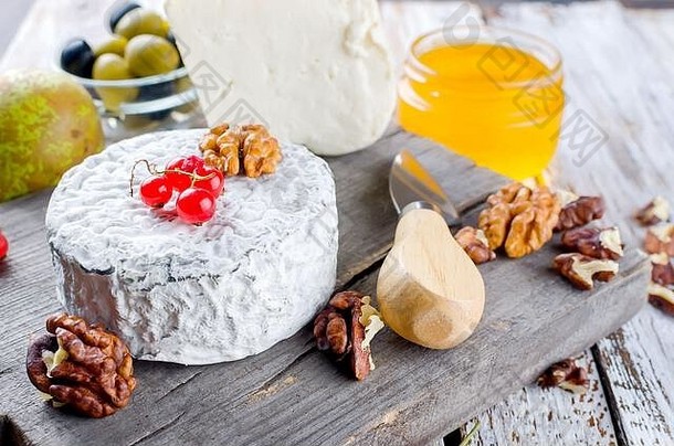 类型美味的奶酪木董事会零食坚果蜂蜜浆果橄榄白色木表格食物成分回来