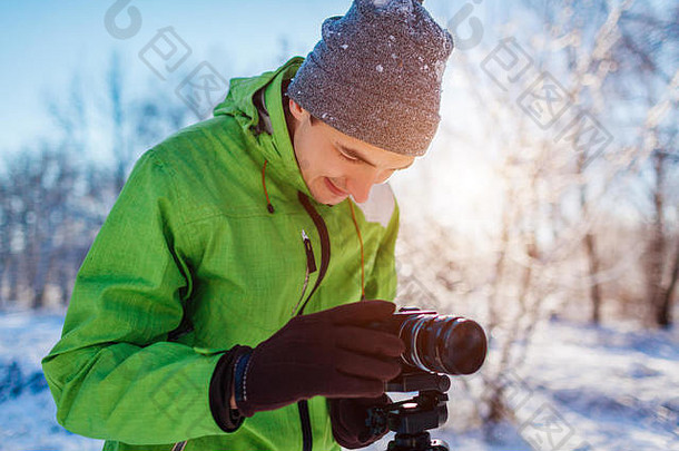 年轻的摄影师需要图片冬天森林相机三脚架年轻的男人。享受爱好在户外