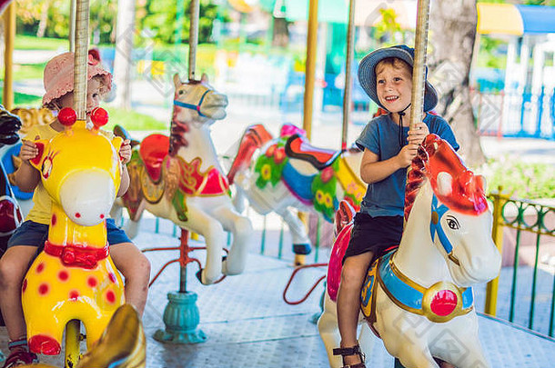 可爱的男孩女孩享受游乐场骑色彩斑斓的旋转木马房子