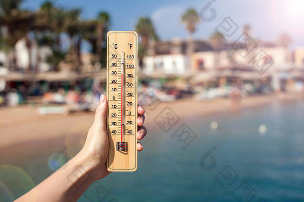 手女人持有温度计海滩背景夏天气候天气概念