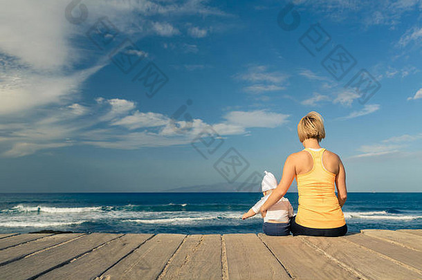 婴儿男孩玩妈妈。海滩夏天一天超级妈妈蹒跚学步的儿子放松木海滩人行道上鼓舞人心的景观