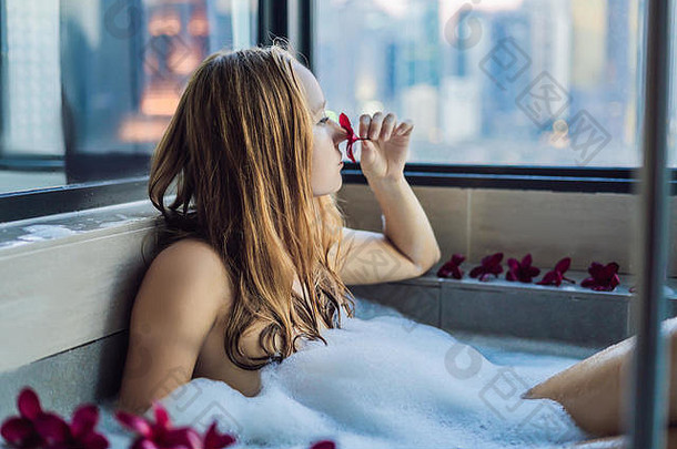 年轻的女人坐在浴泡沫鸡蛋<strong>花花</strong>背景全景窗口俯瞰摩天大楼大晚上