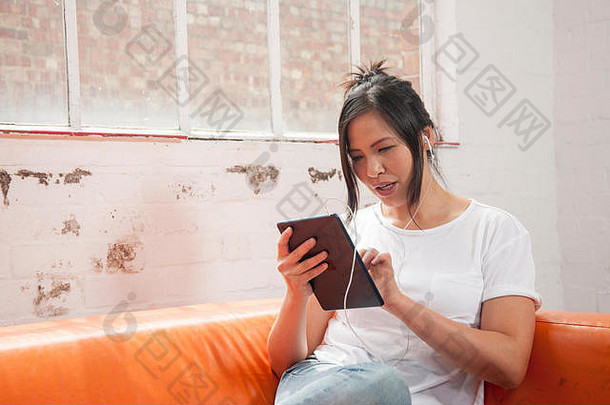 亚洲女人听音乐iPad坐着橙色沙发
