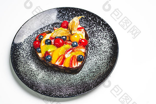 心形状的水果海绵蛋糕水果蛋挞黑色的板撒粉糖健康的糖果背景复制空间