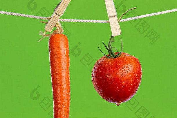 新鲜的洗红色的成熟的番茄<strong>橙色胡萝卜</strong>挂干燥晾衣绳绿色背景