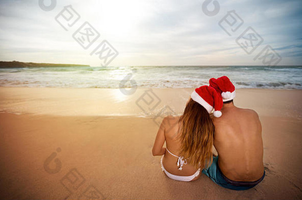 夫妇圣诞老人帽子坐着桑迪海滩回来视图