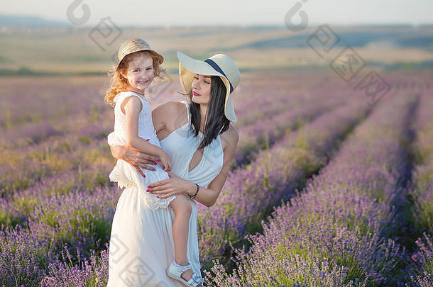 年轻的美丽的夫人妈妈。可爱的女儿走薰衣草场周末一天美妙的礼服帽子