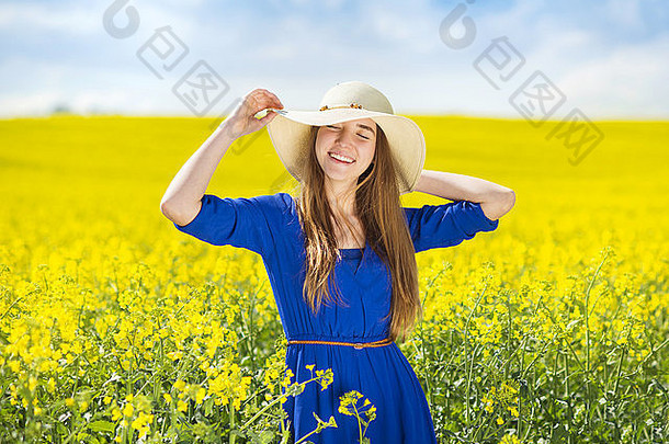 快乐年轻的女孩蓝色的衣服稻草他享受免费的时间黄色的油菜花场