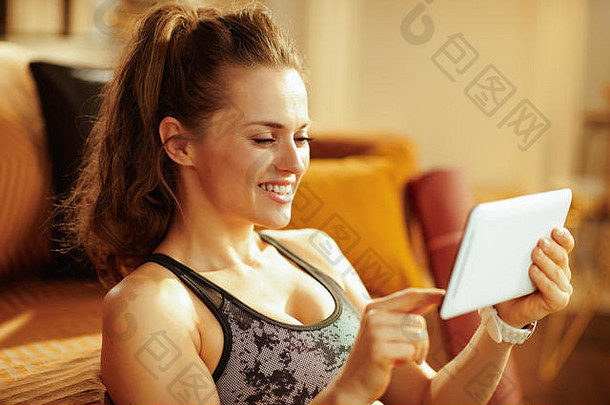 微笑活跃的女人体育运动衣服现代房子看健身教程互联网平板电脑