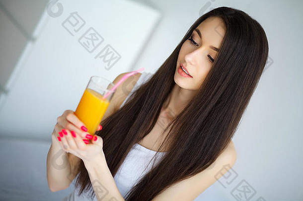 年轻的女人享受玻璃橙色汁早....放松坐着<strong>床</strong>上健康的饮食概念