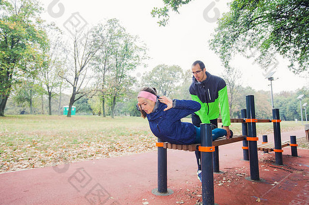 健身年轻的女人俯卧撑帮助朋友设备户外体育公园