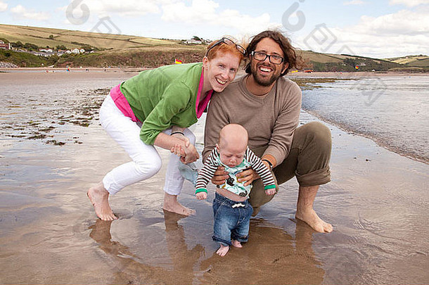 英国德文郡海滩上的一对年轻夫妇和两个月大的。