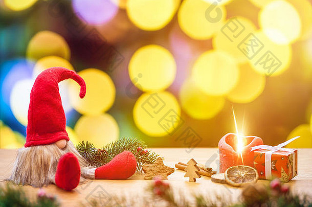 红色坐着的圣诞精灵，背景是波基灯，周围是圣诞装饰品，作为礼品盒，点燃了降临节蜡烛