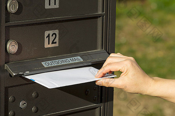 女邮递员将信件放入邮筒的照片，背景为绿草