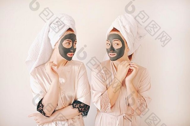 两个穿着浴衣、头上戴着毛巾的年轻女姐妹被隔离在白色背景上。在家做水疗。他们在脸上做了一个护肤面膜