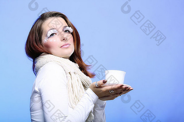 冬季创意化妆白色长睫毛女孩年轻女子用一杯热饮料喝咖啡蓝色晚卡布奇诺