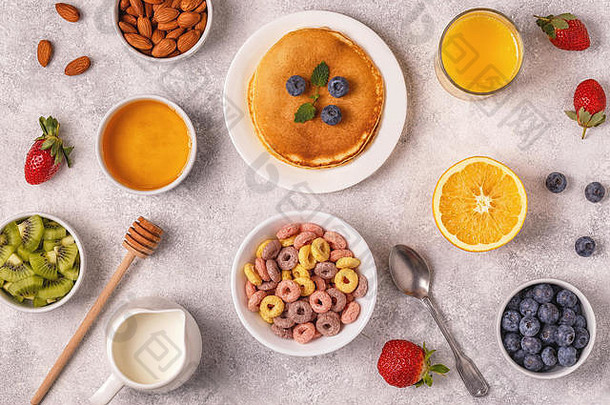 早餐有五颜六色的麦片圈、煎饼、水果、牛奶、果汁。顶视图。